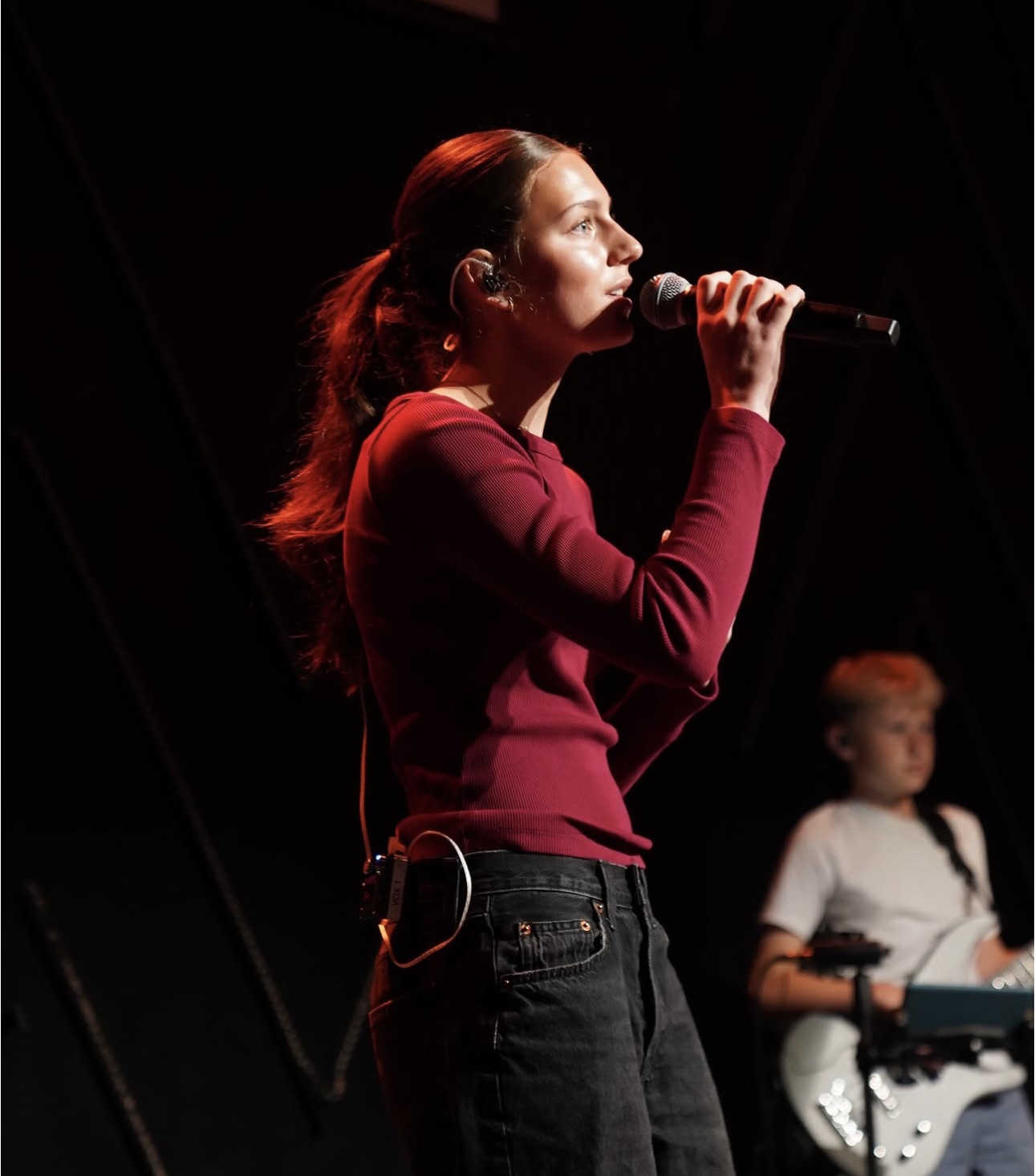 Student vocalist leading worship with a student guitarist in the background